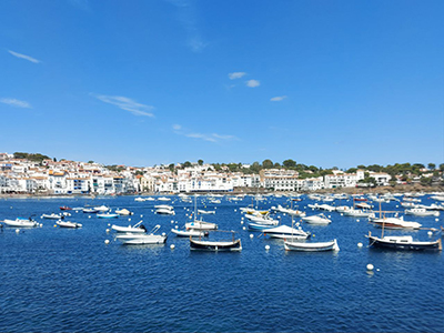 Small fishing boats floating in the blue waters of Cadaqués, with a coastal village in the background